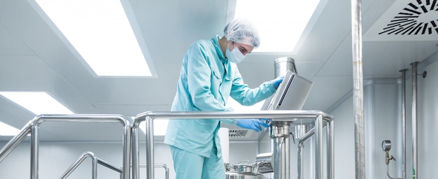 Pharmaceutical factory man worker in protective clothing operate production line in sterile working conditions