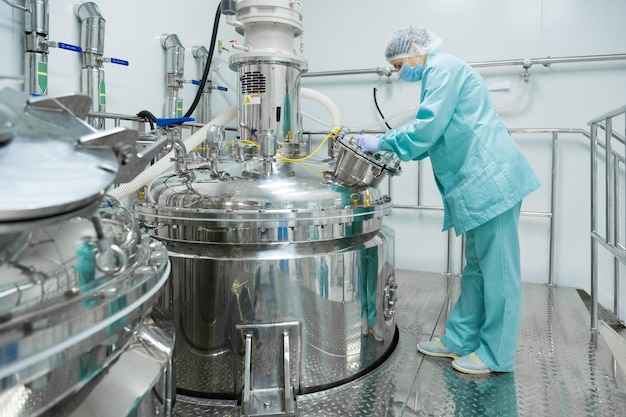 Pharmaceutical factory woman worker in protective clothing operating production line in sterile environment