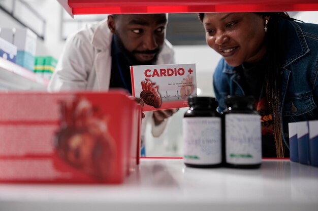 クライアントが心臓薬を選択するのを助ける薬剤師、ドラッグストアの棚の接写、限定フォーカス。タブレットパッケージ、製薬サービスを購入するアフリカ系アメリカ人の満足した顧客