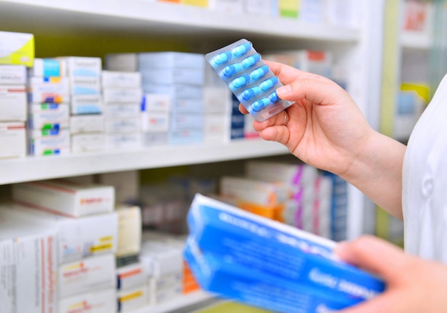 Pharmacist holding medicine box and capsule pack in pharmacy drugstore.