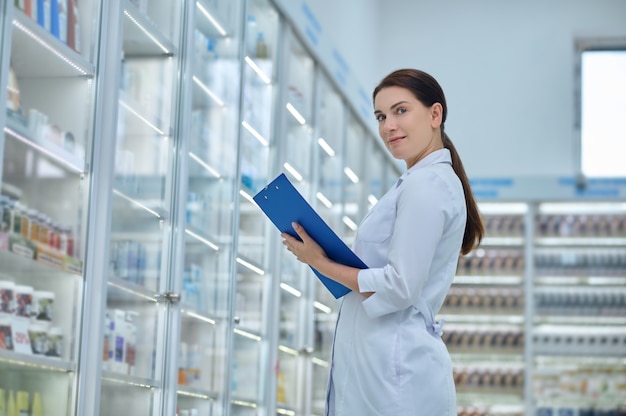 Foto farmacista in posa per la telecamera tra scaffali con prodotti sanitari