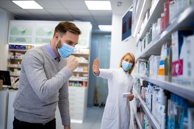 Pharmacist stepping back while sick customer coughing and spreading corona virus in pharmacy shop