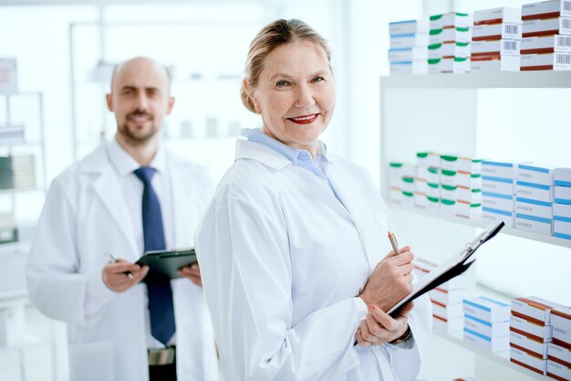 Photo pharmacist with a clipboard and her colleague standing near a pharmacy display case