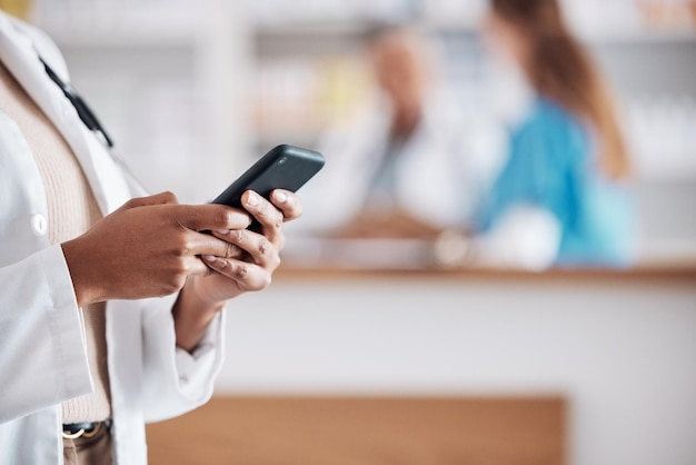 Pharmacist with phone typing in clinic and medical information research email or online chat Smartphone networking and mockup woman doctor in pharmacy checking social media or internet news