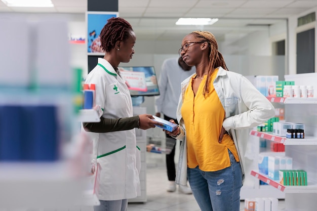 Pharmacy consultant recommending buyer back pain medication.\
african american woman client with backache shopping in drugstore,\
talking with pharmacist in aisle, choosing medicine