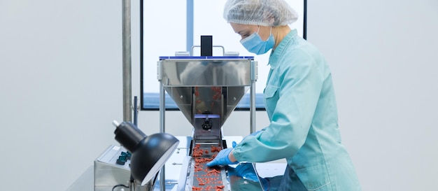 Pharmacy industry woman worker in protective clothing operating production of tablets in sterile working conditions