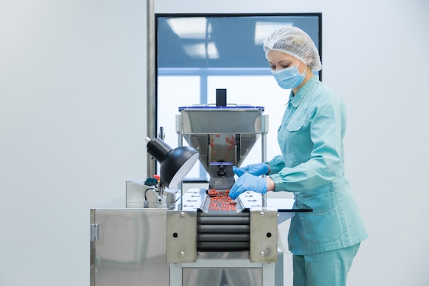 Pharmacy industry woman worker in protective clothing operating production of tablets in sterile working conditions