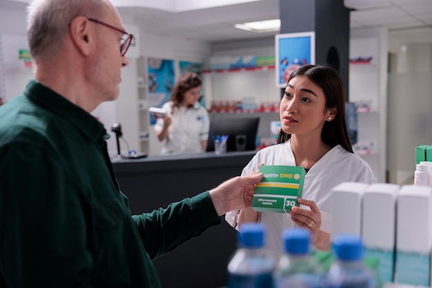 Photo pharmacy worker showing pills package to senior customer during medical consultation explaining prescription. elderly man buying supplements, drugs to cure disease. health care support