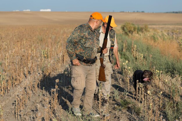 Pheasant hunters with shotgun walking through a meadow.