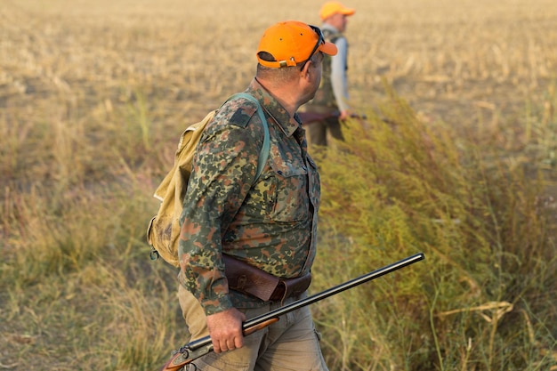 Pheasant hunters with shotgun walking through a meadow