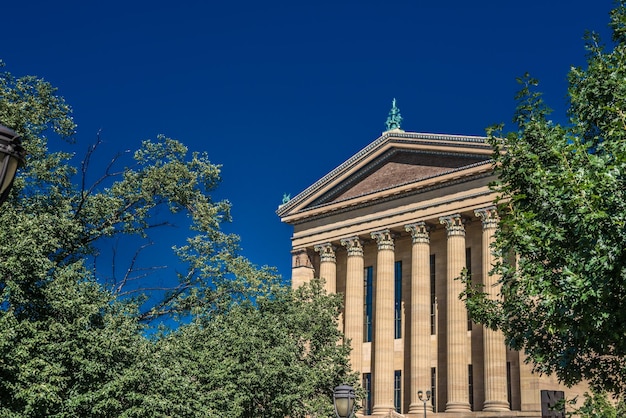Художественный музей Филадельфии сквозь зелень на фоне ясного голубого неба в США