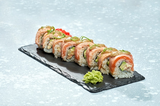 Philadelphia sushi roll with smoked salmon, avocado, cream cheese and sweet sauce on a black plate on a light background