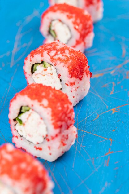 Philadelphia sushibroodjes met verse roomkaas die op blauwe houten raad wordt geplaatst.