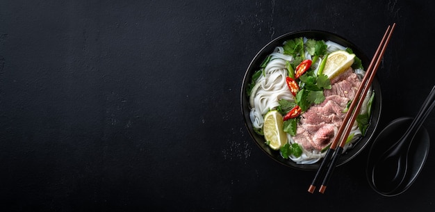 Pho bo zuppa vietnamita con manzo e spaghetti di riso su uno sfondo nero vista dall'alto spazio copia