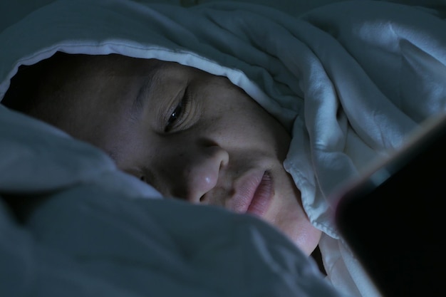 Phone addict concept Asian woman with smart phone on bed can not sleep in the midnight