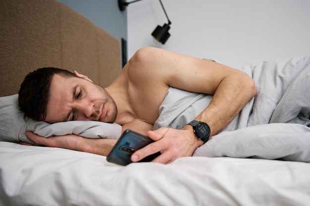 Phone addiction Man lying in bed with smartphone