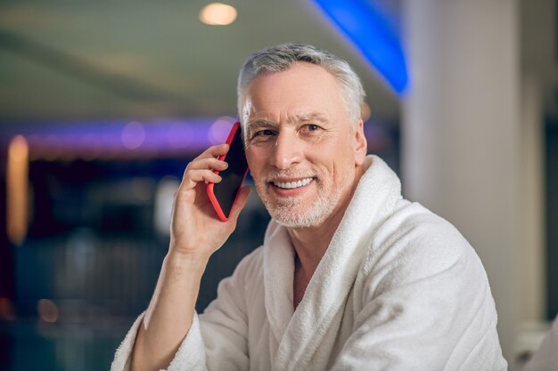 On the phone. Bearded man in a white bath robe in spa center talking on the phone