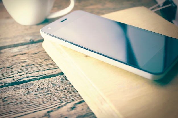 Phone on book and coffee on wooden table