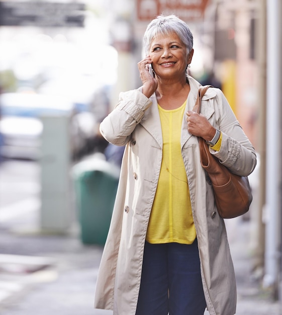 Телефонный звонок, прогулка по городу, и пожилая женщина разговаривает по мобильному телефону, обсуждает общение или общается с пользователем смартфона.