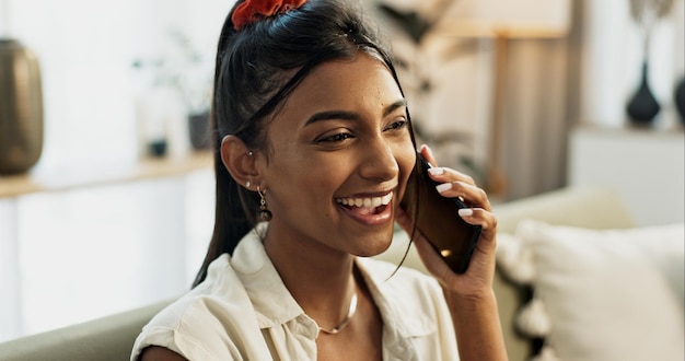 Phone call laughing and young woman on a sofa for relaxing in the living room of apartment Happy smile and Indian female person on mobile conversation with cellphone in lounge of modern home