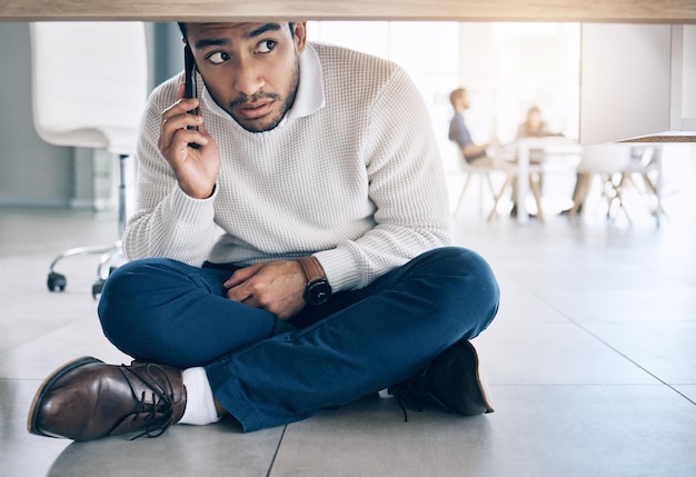 Phone call office and businessman sitting on floor under table with worry fear and scared expression on face Depression anxiety and stressed male worker on smartphone call for help and support