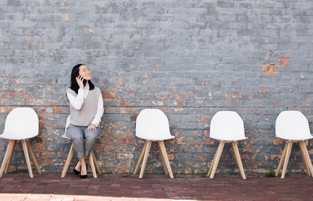 Phone call thinking in waiting room and woman with chairs job recruitment and employment with smile in Japan Happy person sitting on chair with smartphone smiling and talking with mockup space