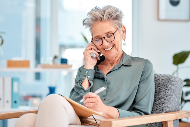 Phone call writing and schedule with a female leader manager or CEO talking while making an appointment in her notebook Mobile communication and diary with a senior business woman writing notes