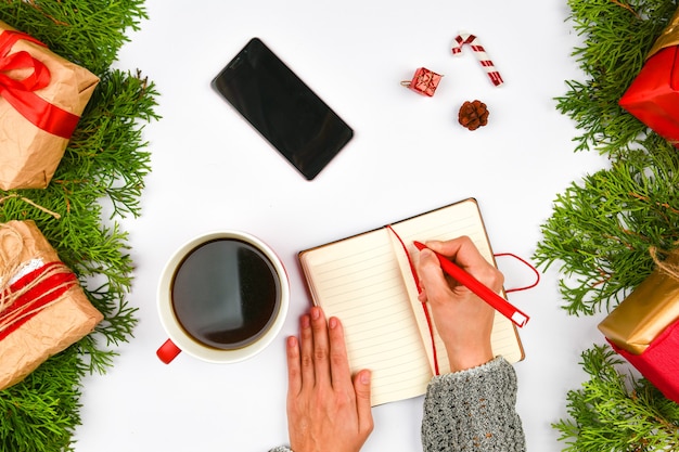 Phone, coffee mug on christmas space. View from above. place for writing. White space. Cozy rest. Latte mug, notebook, pen, phone, gift wrapping. needles.