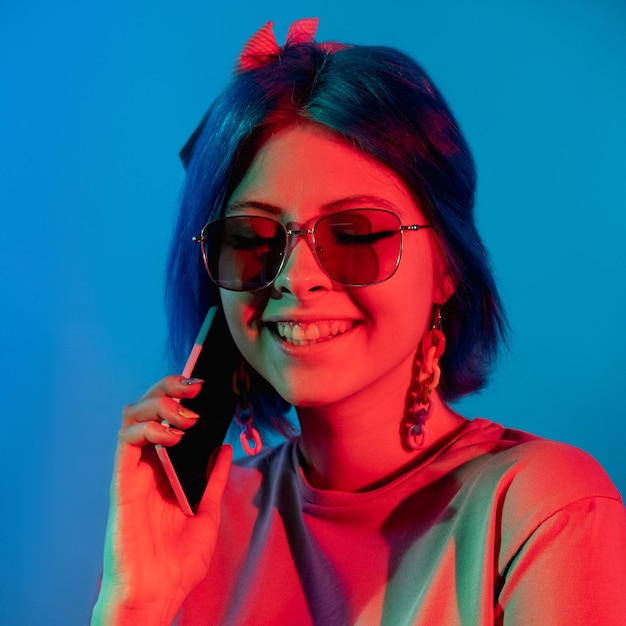 Phone conversation Modern gadget Millennial lifestyle Happy smiling woman in red neon light talking on cellphone isolated on blue background