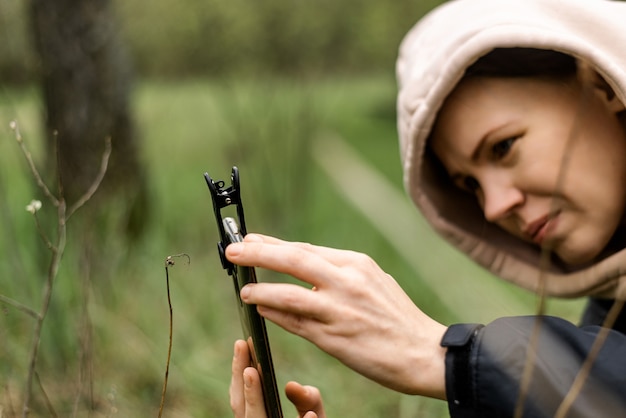 マクロ撮影用の電話レンズ。マクロアタッチメント付きの携帯電話を手に持った女性が、植物の写真を撮ります。