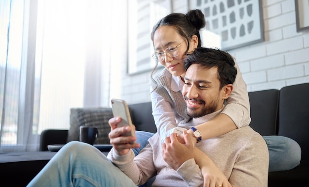 Phone love and diversity with a couple in their home bonding while browsing social media in the living room Mobile communication or internet with an interracial man and woman together in a house