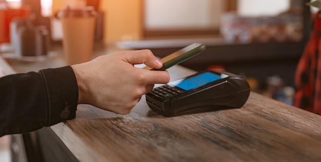 Primo piano del pagamento telefonico di un cliente che collega uno smartphone a un terminale di pagamento per pagare un caffè in un bar