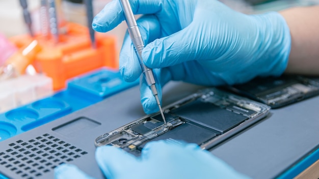 Phone repair concept a bare hand holding tweezers gripping a tiny part in a circuit board carefully and precisely on the wooden desk