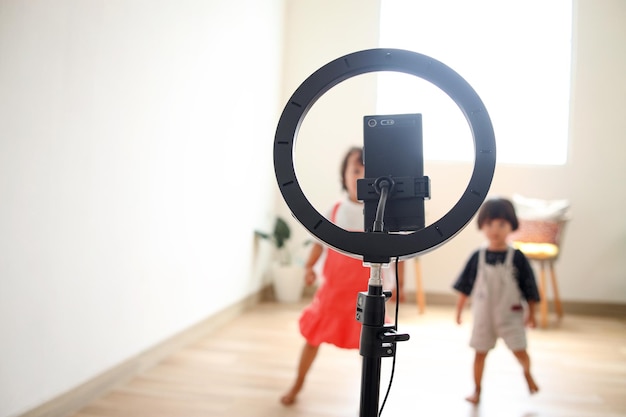 Phone on rim light tripod with blurry Asian children dancing at camera filming video