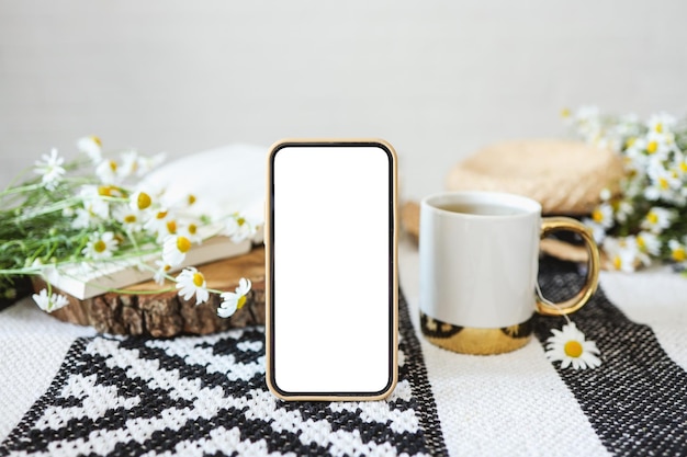 Phone screen with an isolated screen on the background of a cup\
of tea a book and daisies a place for your text