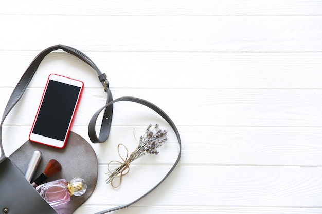 Phone, stylish bag and perfumes on white background. Beautiful flat lay. Things for business woman. Note book schedule. Makeup kit. Lavender bouquet.