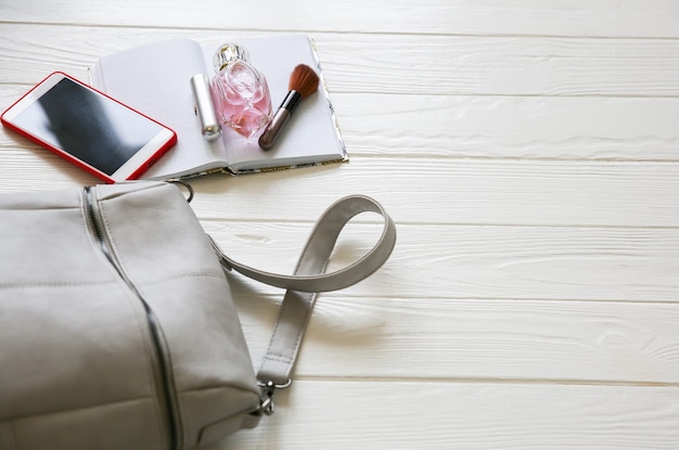 Telefono, borsa elegante e profumi su sfondo bianco. bella disposizione piatta. cose per donna d'affari. agenda del taccuino. kit del make up.