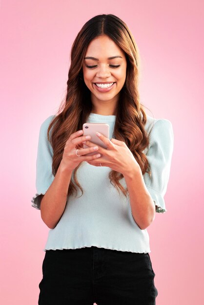ピンクの背景にソーシャルメディアやアプリをオンラインで通信するためのスタジオでの電話テキストメッセージと幸せな女性インターネットスマートフォンとストリーミングサブスクリプションまたはウェブサイト検索を分離した女の子の笑顔
