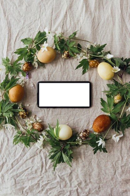 Phone with blank screen in easter rustic wreath with eggs and flowers flat lay Seasons greetings