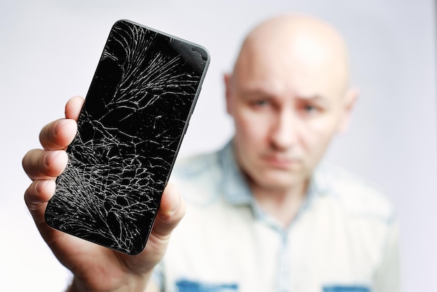 Phone With A broken screen closeup A white man is holding a black smartphone with a cracked display