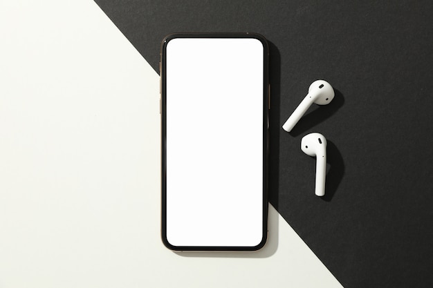 Photo phone with empty screen and headphones on black - white background, top view