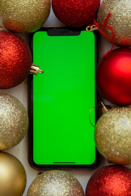 Photo a phone with a green screen lies among the golden and red christmas balls high quality photo