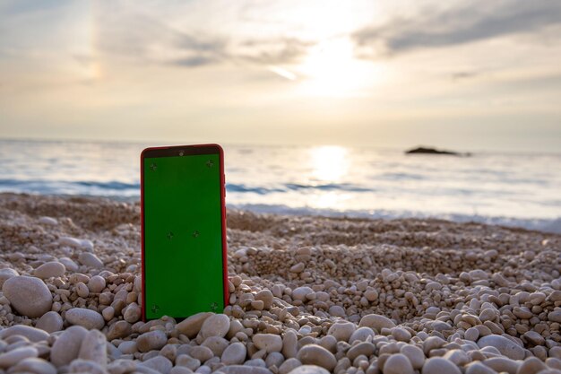 Phone with green screen at rocky sea beach on sunset