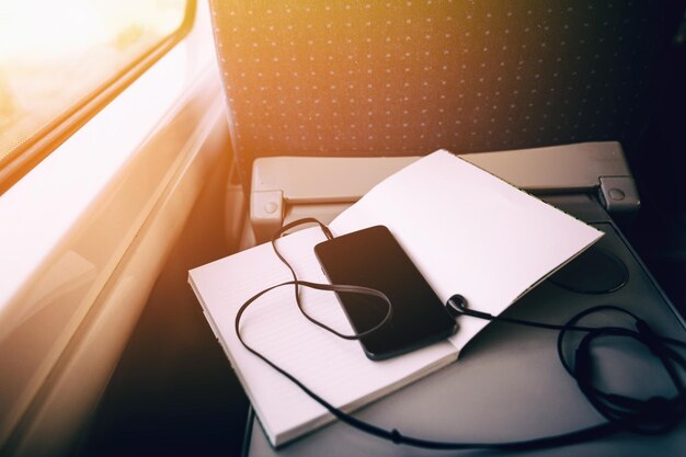 Phone with headphones on notebook at window light in train\
smartphone empty screen on table space for text travel and\
transportation concept social media communication