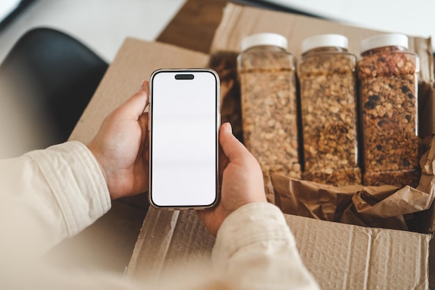 Phone with an isolated screen in hands against the background of a parcel with granola