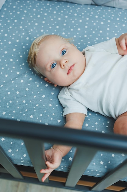 Photo of a 5monthold baby lying in a crib A cot with a little boy in a white bodysuit