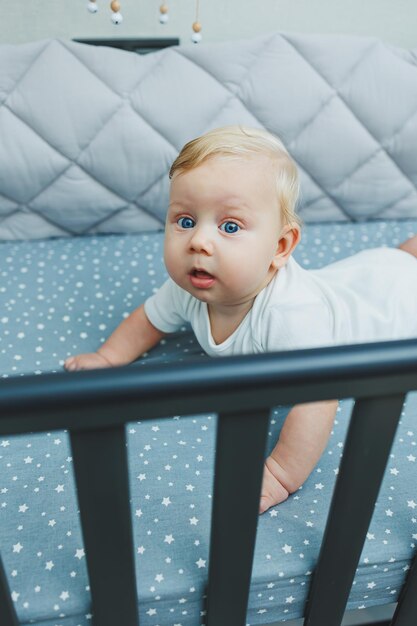 Photo of a 5monthold baby lying in a crib A cot with a little boy in a white bodysuit