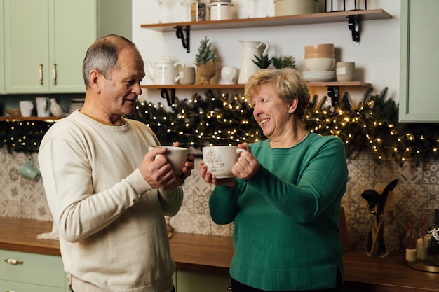 Photo of 60s elderly couple enjoying life at the kitchen with mugs of coffee. st valentines day of old couples in love. stop ageism discrimination. High quality photo