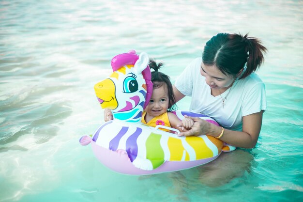 Photo of adorable little girl with mom Colorful unicorn inflatable ring swimming in a tropical ocean on summer vacation High quality photo copy space for text