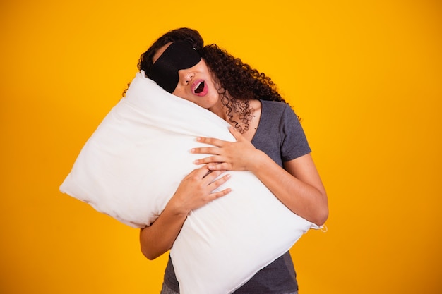 Foto foto di una ragazza afro che abbraccia il cuscino su sfondo giallo. primo piano della ragazza che tiene un cuscino nelle sue mani. concetto di sonno